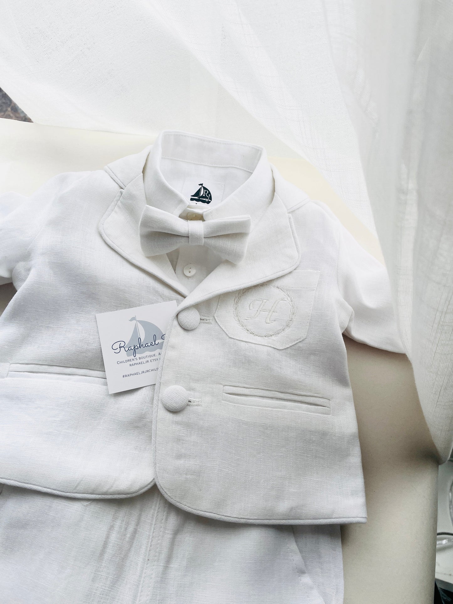 White linen suit with jacket, shirt, pants, and white bowtie, white stitching on jacket pocket.