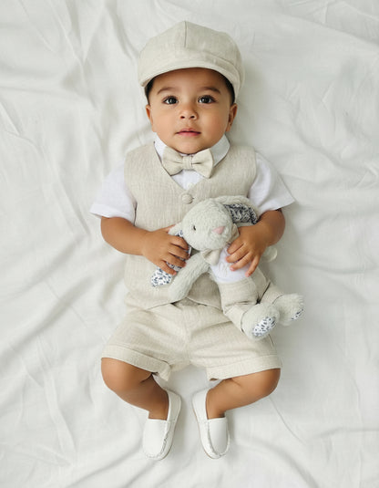 Baby in formal outfit holding a teddy bear on a white background