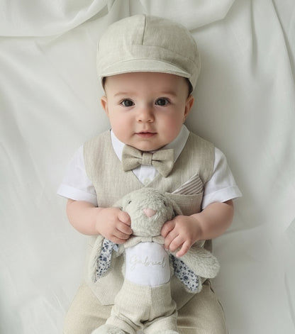 Children's beige linen Baptismal outfit with vest, hat, and shoes on a white blanket and a bunny soft toy
