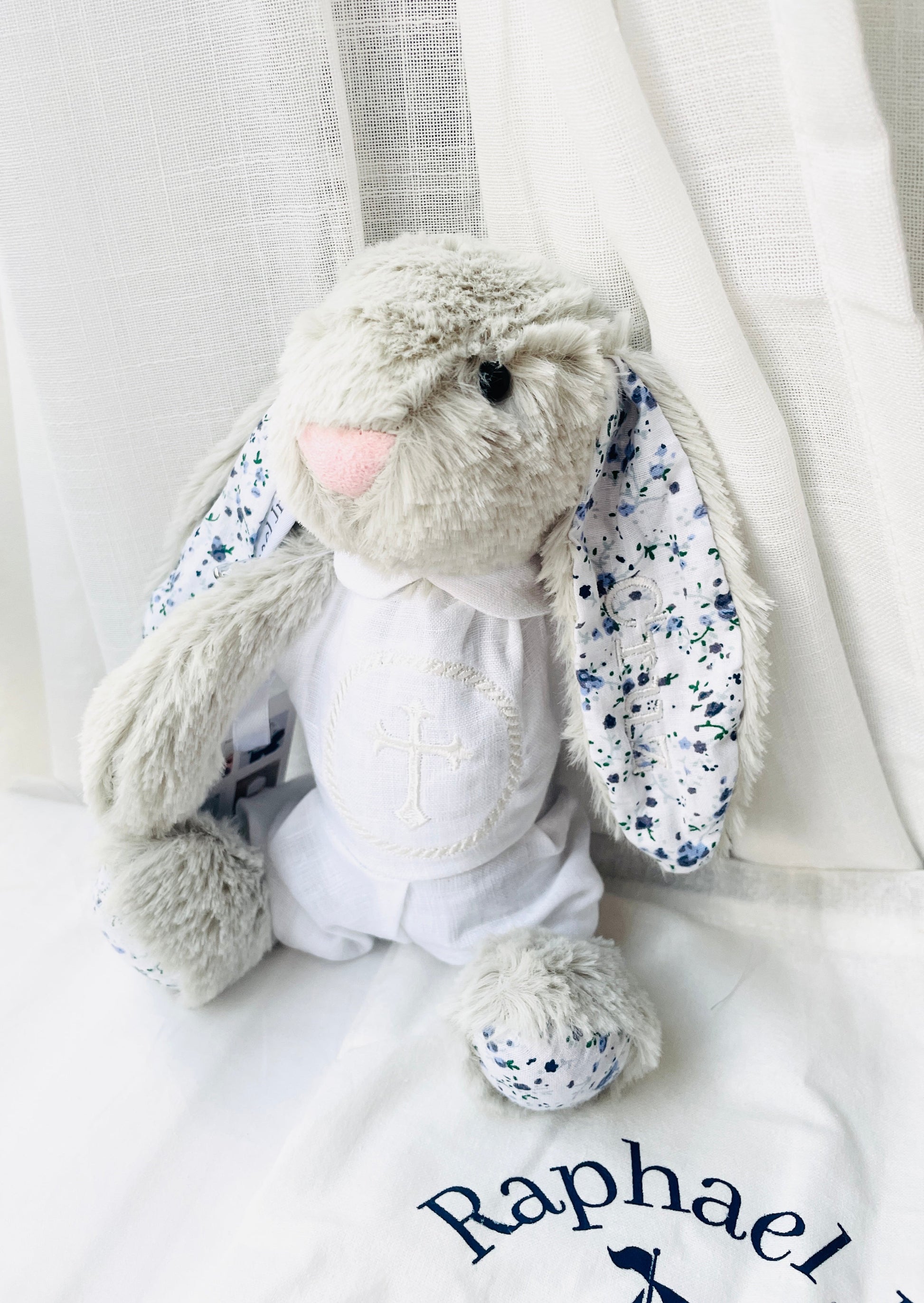 light grey fluffy bunny toy with floral ears, stitching in right ear saying Cruz.